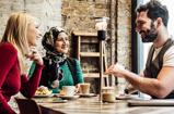 Three people drinking coffee at a table.