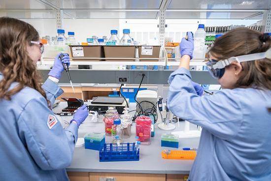 two people in lab coats inject things into test tubes in lab setting